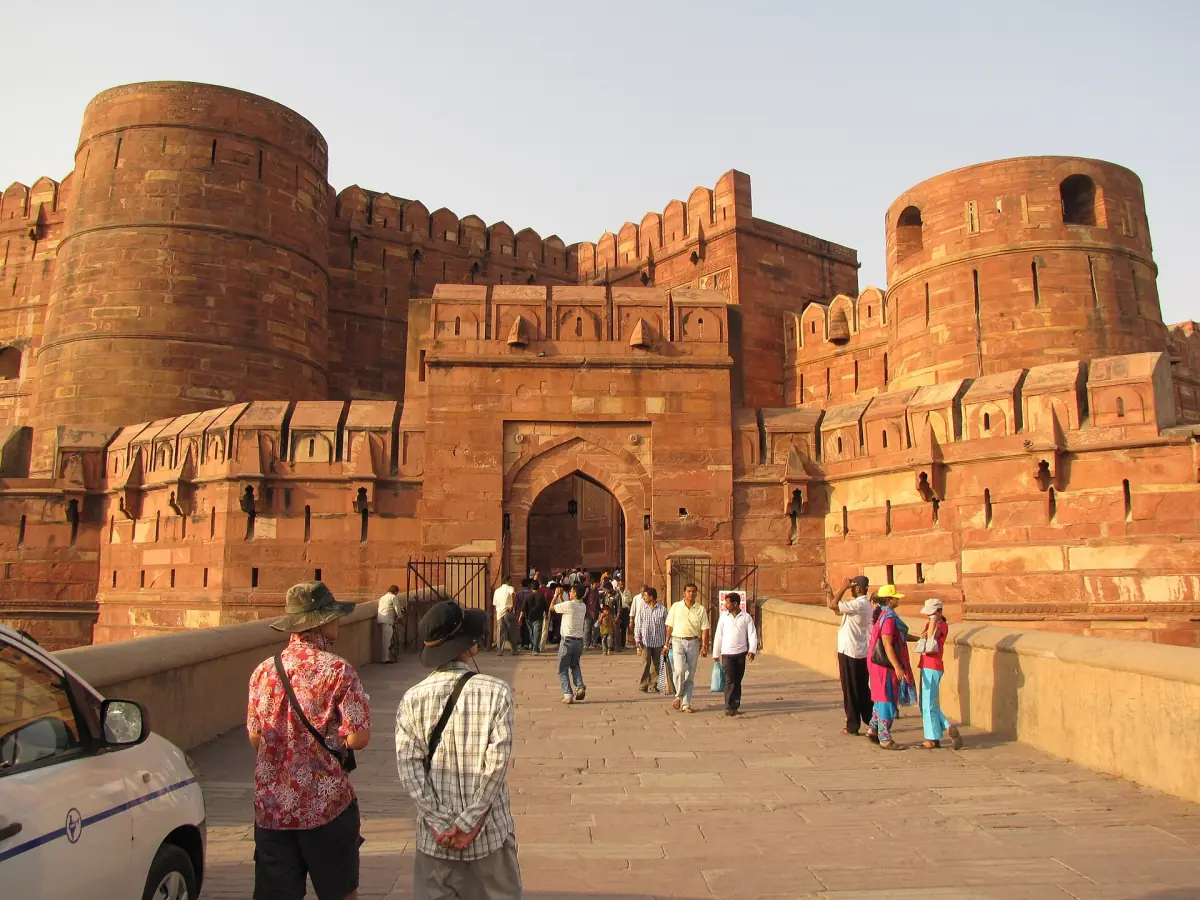 Visitors walking toward the red sandstone gate of Agra Fort in golden light