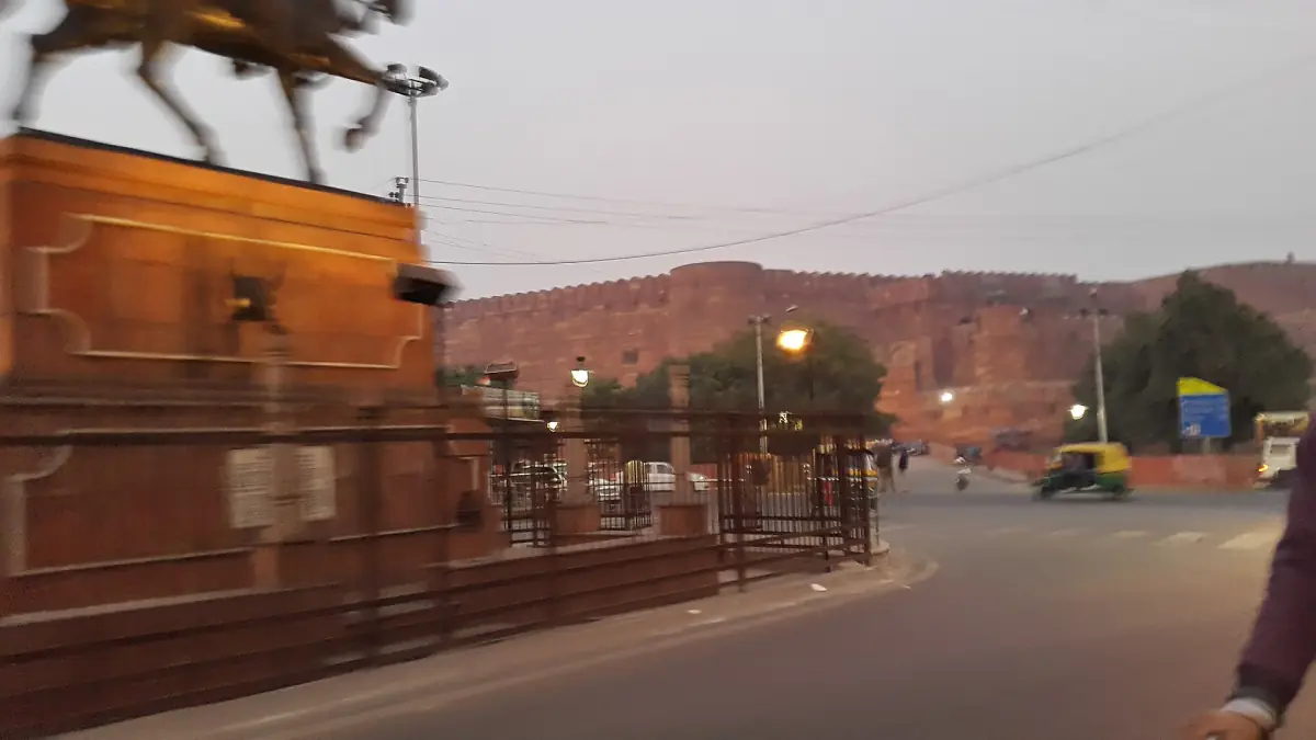 Agra Fort wall glowing at dusk behind a busy road with rickshaws
