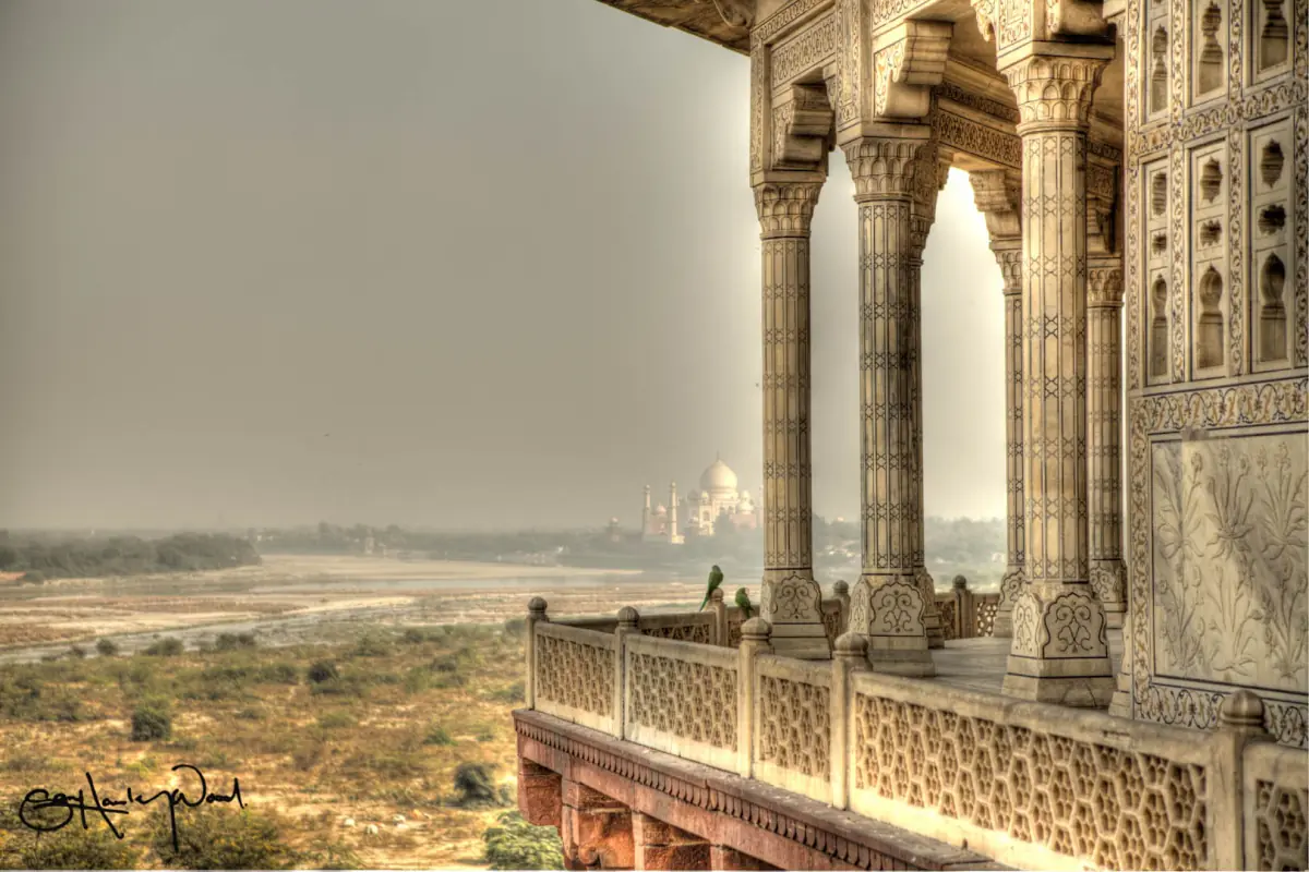 Carved marble pavilion of Musamman Burj framing a hazy distant view toward the Taj Mahal