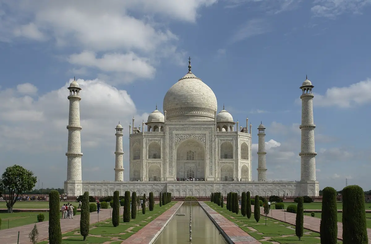 Taj Mahal with its minarets, reflecting pool and cypress trees under scattered clouds